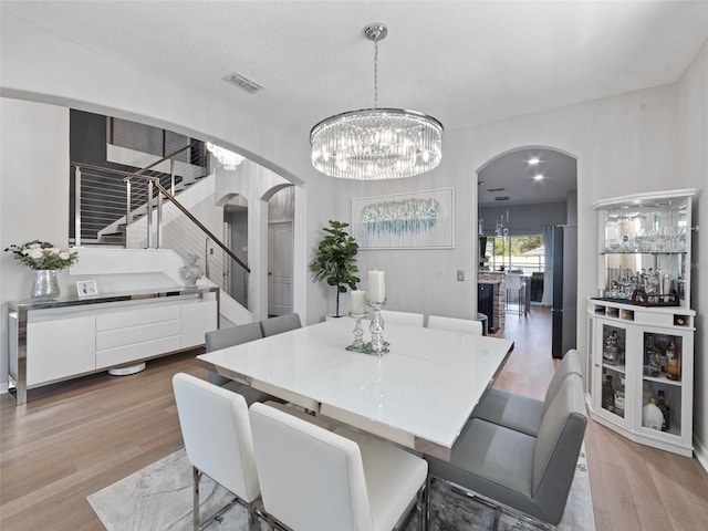 dining room featuring visible vents, stairs, arched walkways, and wood finished floors