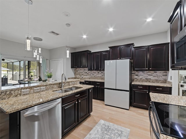 kitchen with light wood-style flooring, stainless steel appliances, a sink, decorative backsplash, and a center island with sink