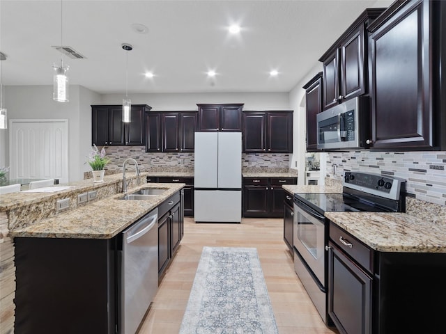 kitchen featuring light stone countertops, appliances with stainless steel finishes, a sink, and decorative light fixtures