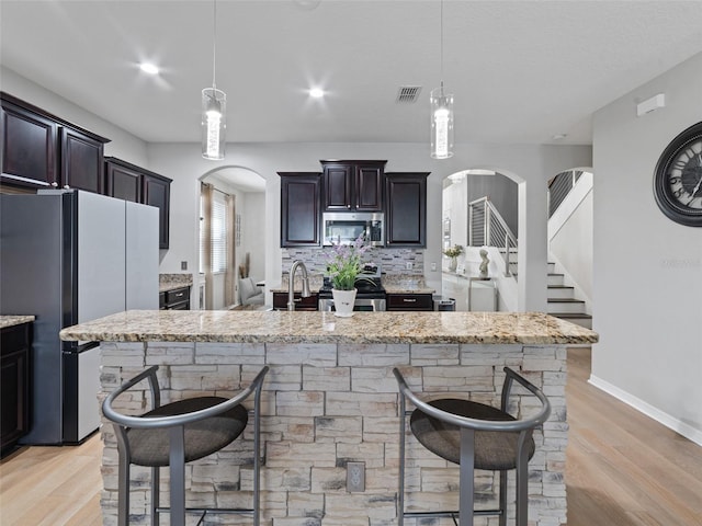 kitchen featuring light stone counters, arched walkways, tasteful backsplash, appliances with stainless steel finishes, and light wood-type flooring