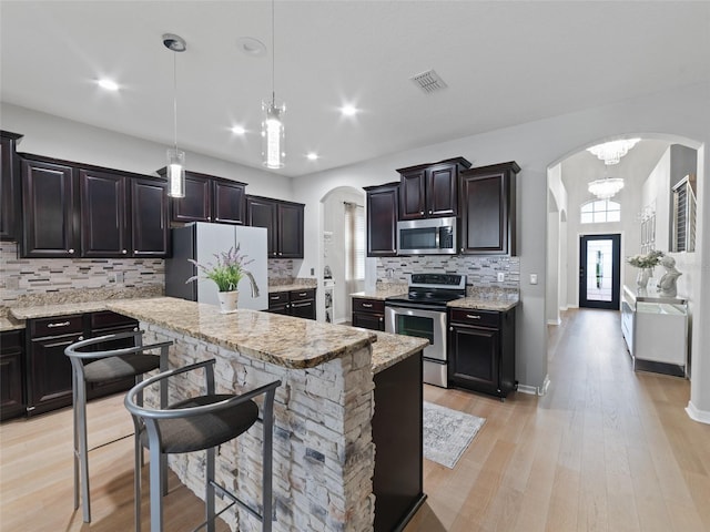 kitchen featuring tasteful backsplash, arched walkways, appliances with stainless steel finishes, hanging light fixtures, and light wood-type flooring