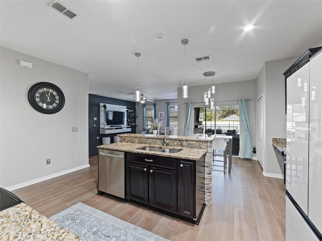 kitchen with light wood finished floors, visible vents, an island with sink, stainless steel dishwasher, and a sink