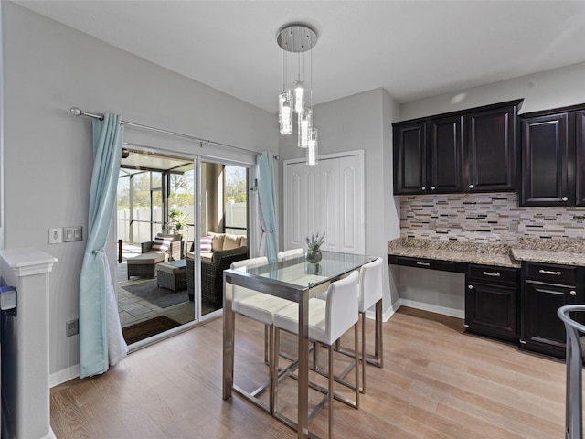 kitchen with light wood finished floors, tasteful backsplash, light stone counters, and dark cabinetry