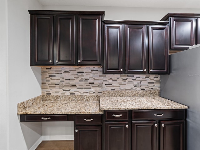 kitchen featuring baseboards, dark brown cabinets, backsplash, freestanding refrigerator, and light stone countertops