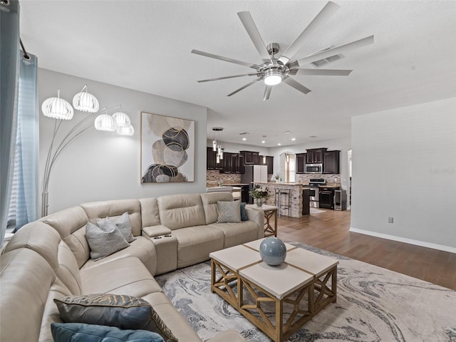 living area with a textured ceiling, wood finished floors, visible vents, baseboards, and a ceiling fan