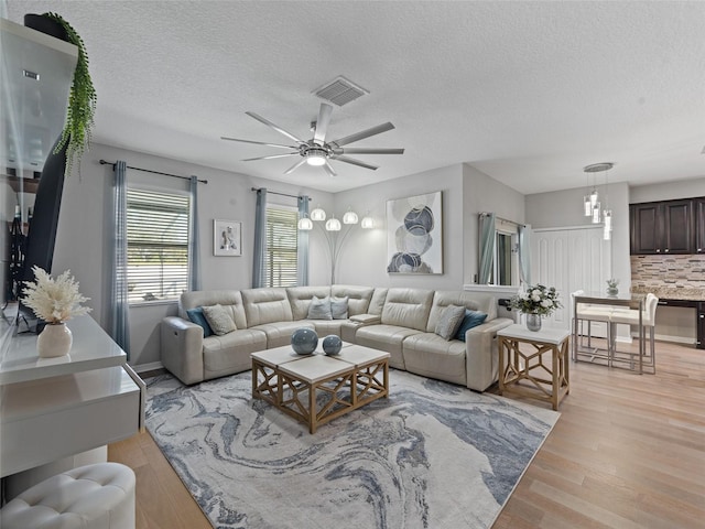 living area with a ceiling fan, visible vents, light wood-style flooring, and a textured ceiling