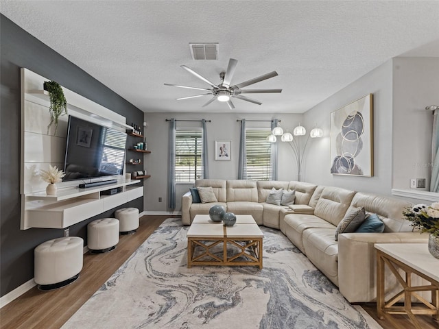 living area with a textured ceiling, ceiling fan, wood finished floors, visible vents, and baseboards