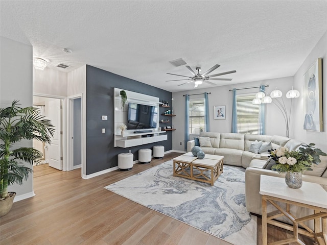 living room featuring a textured ceiling, wood finished floors, visible vents, and a ceiling fan