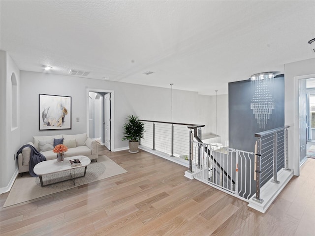 interior space with visible vents, wood finished floors, a chandelier, and an upstairs landing