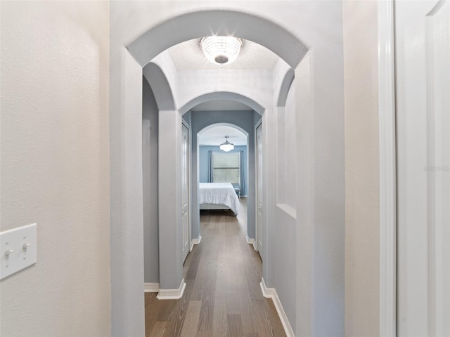 corridor featuring arched walkways, baseboards, and wood finished floors