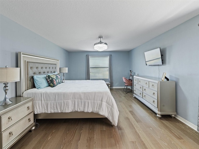 bedroom with a textured ceiling, wood finished floors, and baseboards