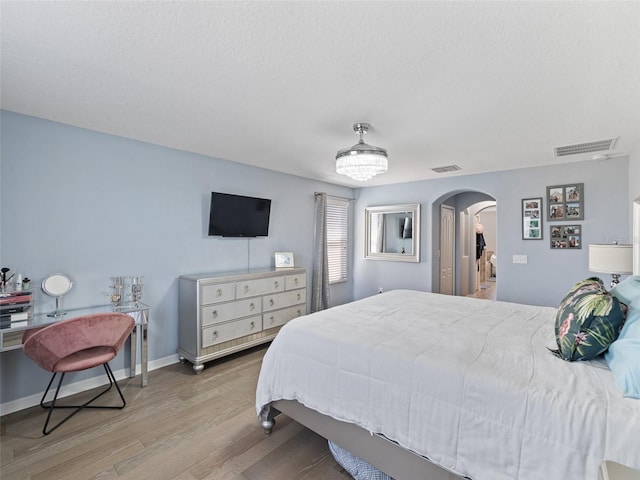 bedroom featuring arched walkways, visible vents, baseboards, and wood finished floors