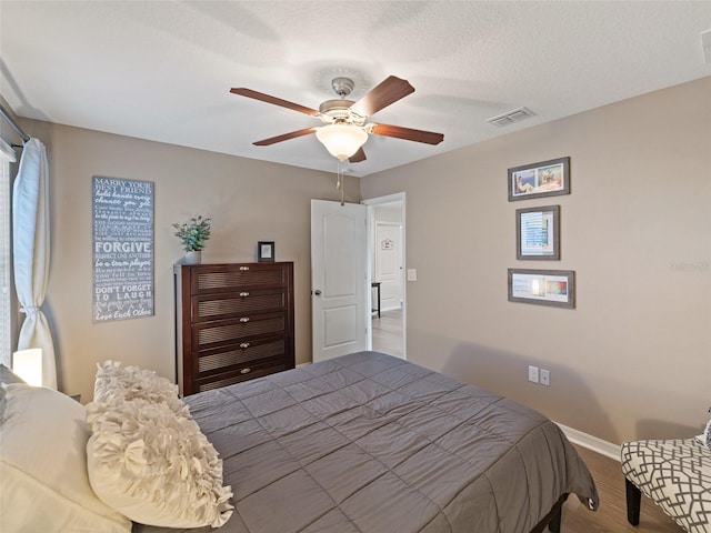 bedroom with visible vents, ceiling fan, a textured ceiling, wood finished floors, and baseboards