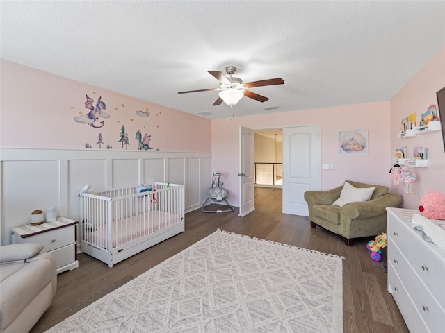 bedroom featuring ceiling fan, visible vents, wood finished floors, and wainscoting