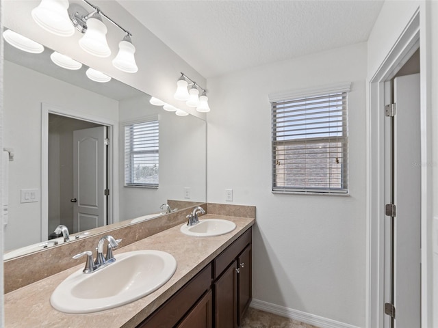 full bath with a textured ceiling, double vanity, a sink, and baseboards