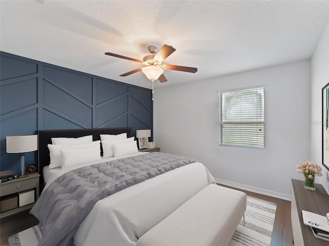 bedroom with a ceiling fan, a decorative wall, a textured ceiling, and wood finished floors