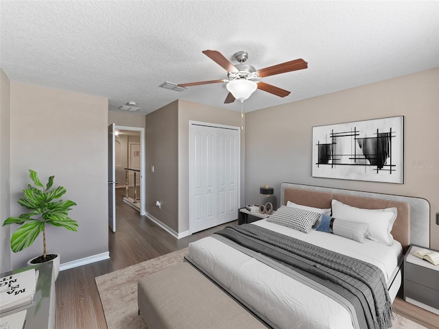 bedroom with a closet, ceiling fan, a textured ceiling, wood finished floors, and baseboards