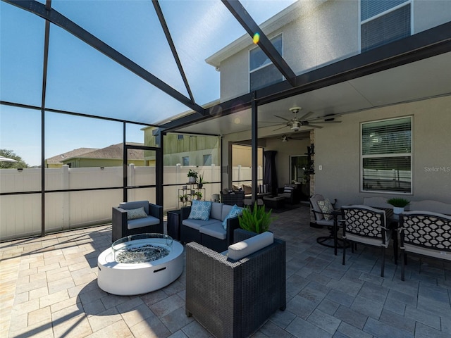 view of patio / terrace with a lanai, ceiling fan, fence, and an outdoor living space with a fire pit