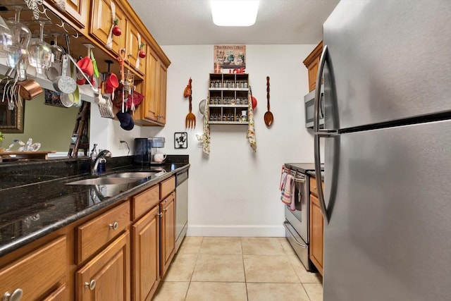 kitchen with light tile patterned floors, stainless steel appliances, brown cabinetry, a sink, and baseboards