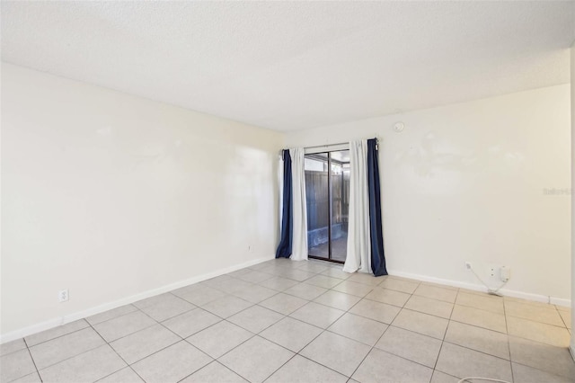 spare room featuring a textured ceiling, baseboards, and light tile patterned floors