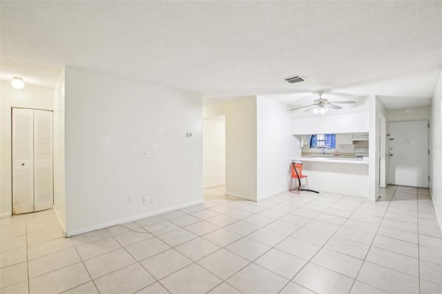 spare room featuring ceiling fan, a textured ceiling, light tile patterned flooring, visible vents, and baseboards