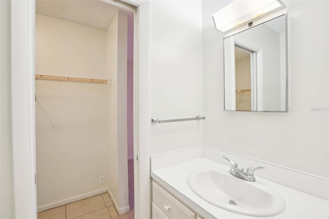 bathroom with a spacious closet, tile patterned flooring, vanity, and baseboards