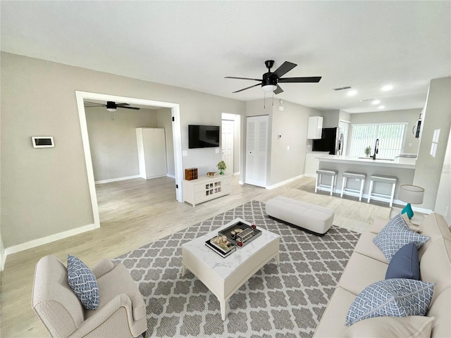 living room with light wood-style floors, ceiling fan, and baseboards