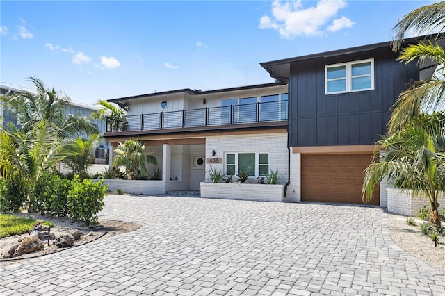 view of front of property featuring decorative driveway, brick siding, an attached garage, board and batten siding, and a balcony