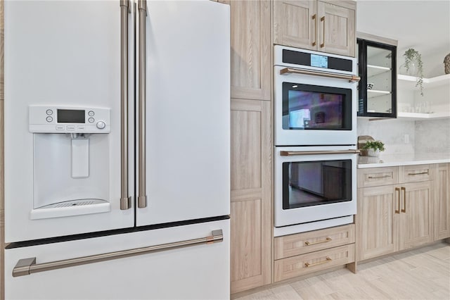 kitchen with light brown cabinets, light wood-style flooring, white appliances, light countertops, and decorative backsplash