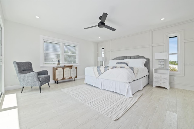 bedroom with multiple windows, light wood-type flooring, a ceiling fan, and a decorative wall