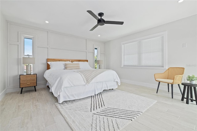 bedroom featuring baseboards, ceiling fan, light wood-style flooring, a decorative wall, and recessed lighting