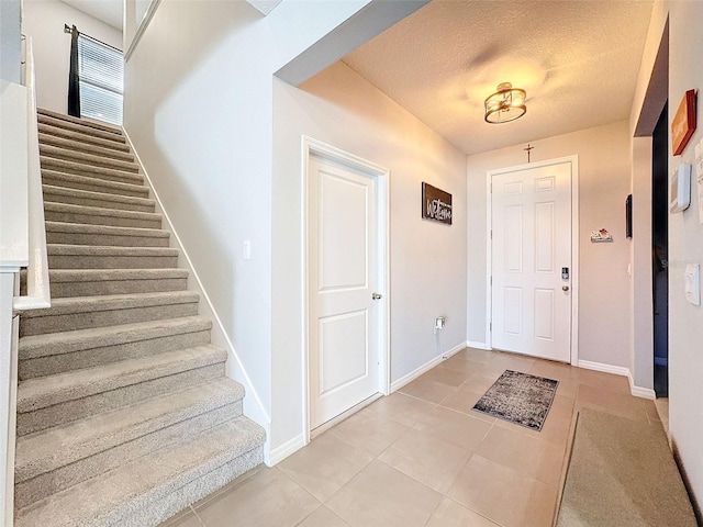 entrance foyer featuring light tile patterned floors, baseboards, stairway, and a textured ceiling