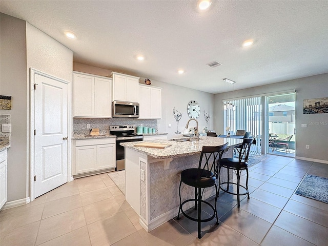 kitchen featuring an island with sink, a kitchen breakfast bar, a sink, stainless steel appliances, and backsplash