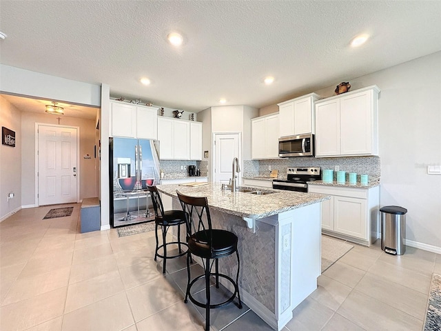 kitchen with a breakfast bar area, decorative backsplash, appliances with stainless steel finishes, a kitchen island with sink, and a sink