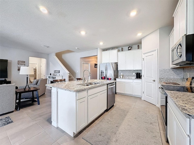 kitchen featuring stainless steel appliances, a sink, white cabinetry, open floor plan, and backsplash