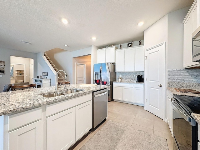 kitchen featuring stainless steel appliances, decorative backsplash, white cabinetry, a sink, and light stone countertops