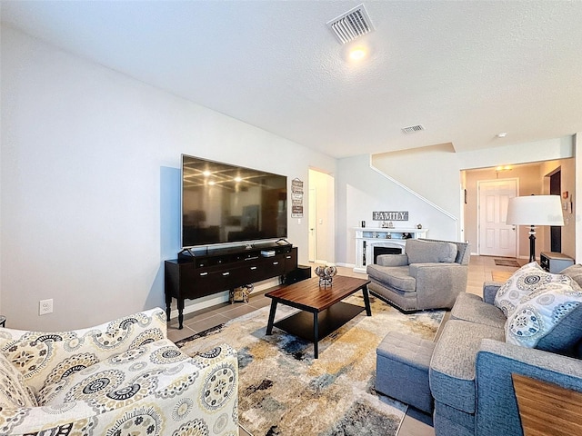 tiled living room featuring a fireplace, visible vents, and a textured ceiling