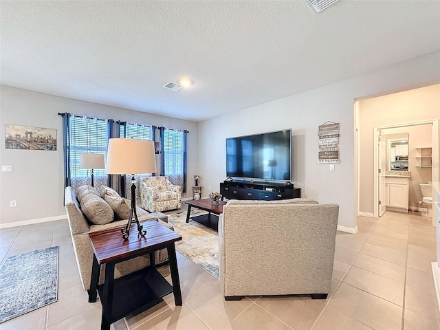 living area featuring visible vents, light tile patterned flooring, a textured ceiling, and baseboards