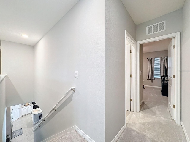 hall featuring baseboards, visible vents, light colored carpet, and an upstairs landing