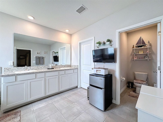 bathroom with toilet, double vanity, a sink, and visible vents