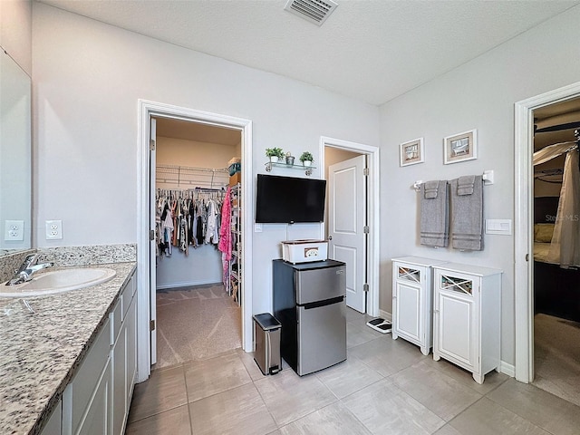 bathroom with vanity, a walk in closet, visible vents, and baseboards