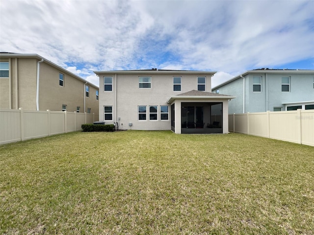 back of house featuring a sunroom, a fenced backyard, a lawn, and stucco siding