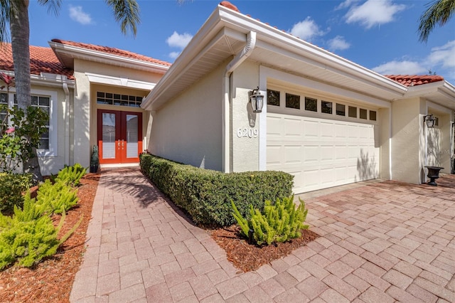 view of exterior entry with stucco siding, decorative driveway, french doors, a garage, and a tiled roof