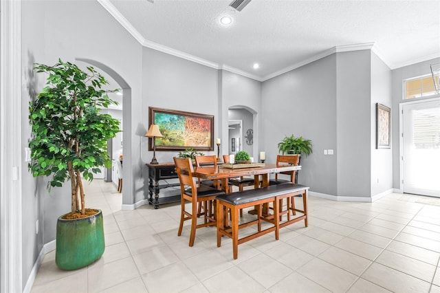 dining area featuring ornamental molding, a textured ceiling, arched walkways, light tile patterned floors, and baseboards