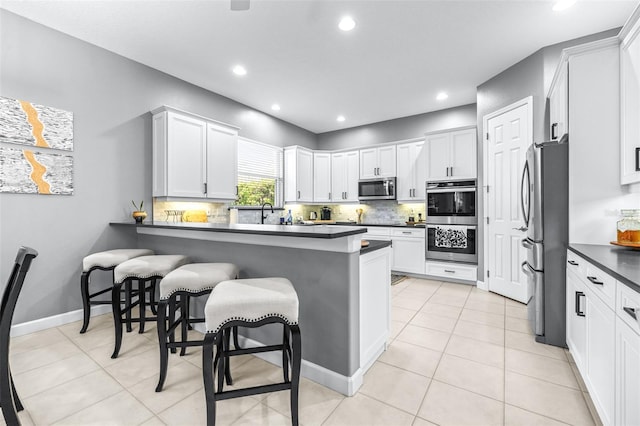 kitchen with dark countertops, stainless steel appliances, a peninsula, a breakfast bar area, and light tile patterned floors