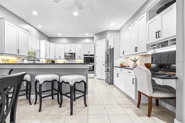 kitchen featuring a sink, dark countertops, appliances with stainless steel finishes, a breakfast bar area, and light tile patterned floors