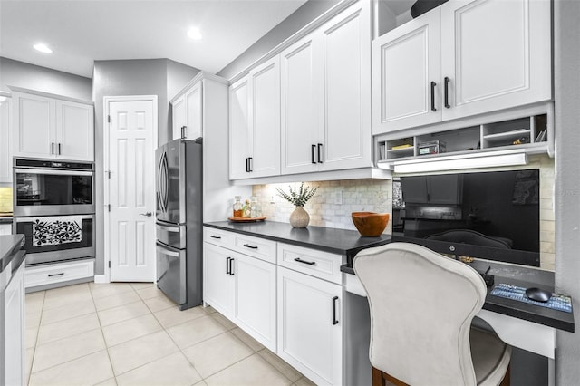 kitchen featuring backsplash, dark countertops, built in desk, appliances with stainless steel finishes, and light tile patterned flooring