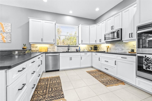 kitchen featuring dark countertops, backsplash, a peninsula, stainless steel appliances, and a sink