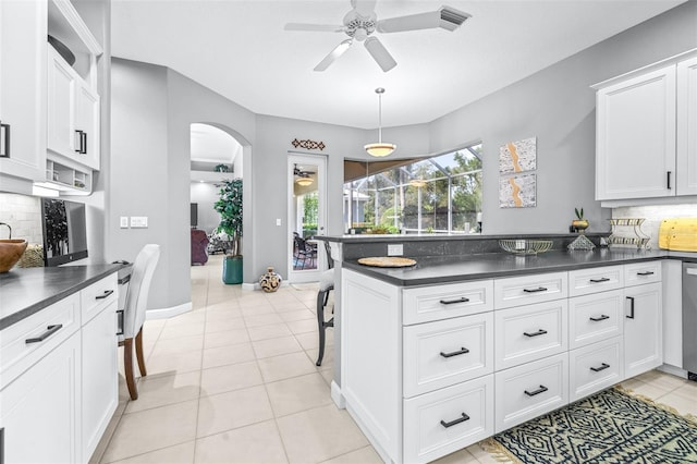 kitchen featuring light tile patterned floors, a peninsula, arched walkways, decorative backsplash, and dark countertops