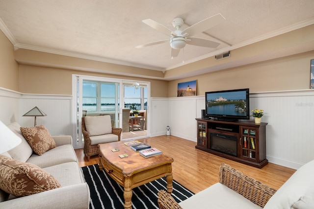 living area with a wainscoted wall, wood finished floors, visible vents, and ornamental molding